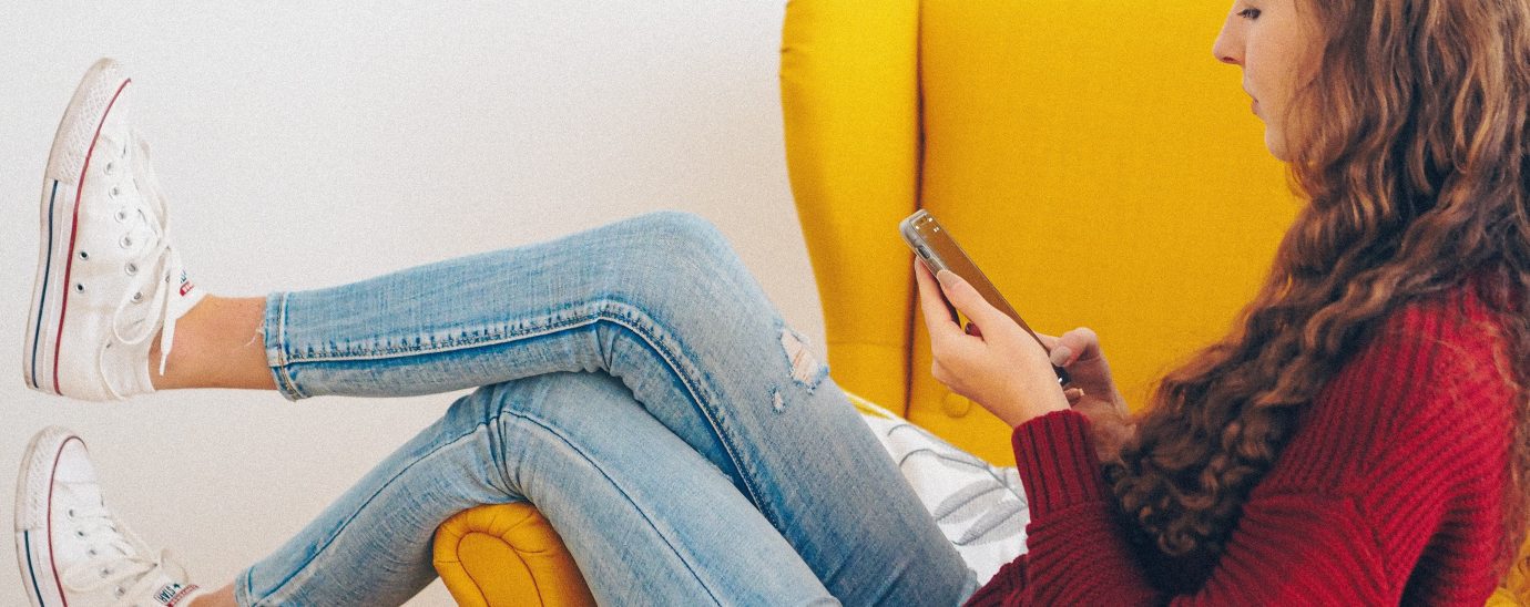 Image of a woman on her phone sitting on a sofa